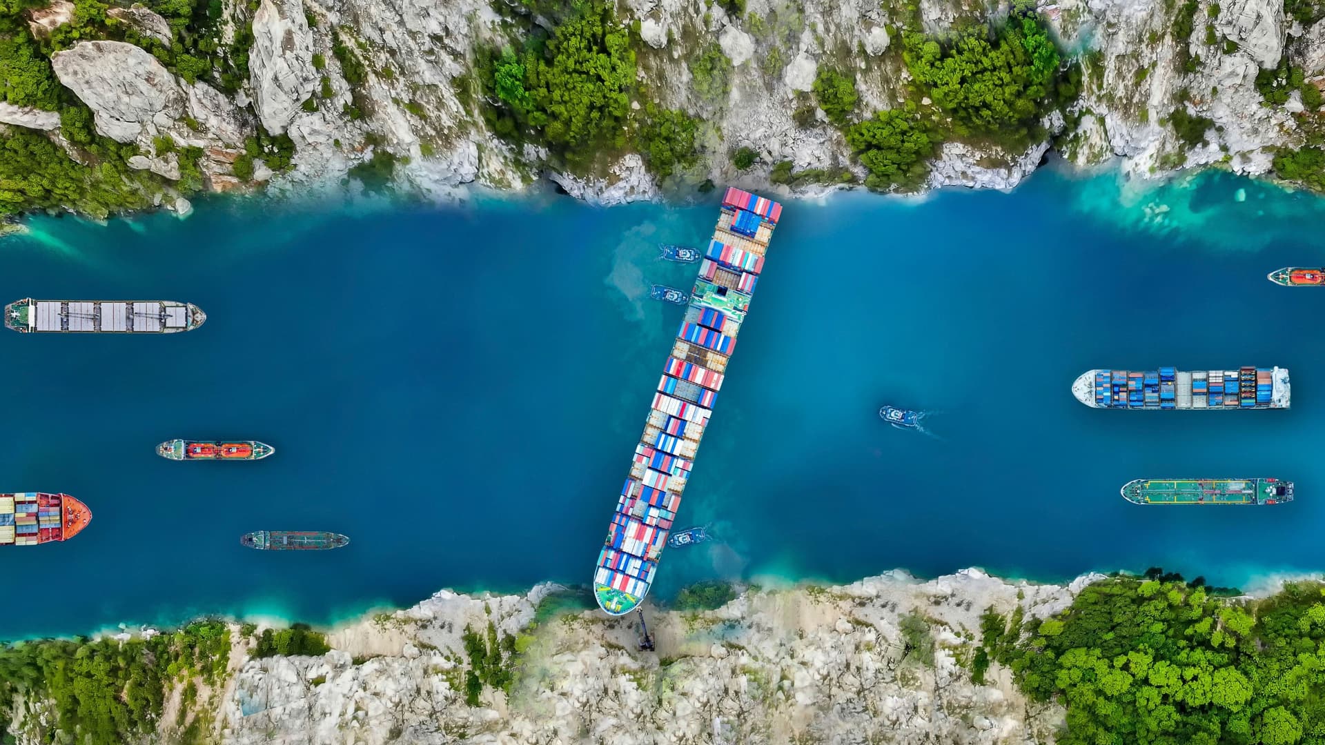 Luftaufnahme eins großes Frachtschiffs das quer in einem Kanal stecken geblieben ist und die Durchfahrt für andere Schiffe blockiert.