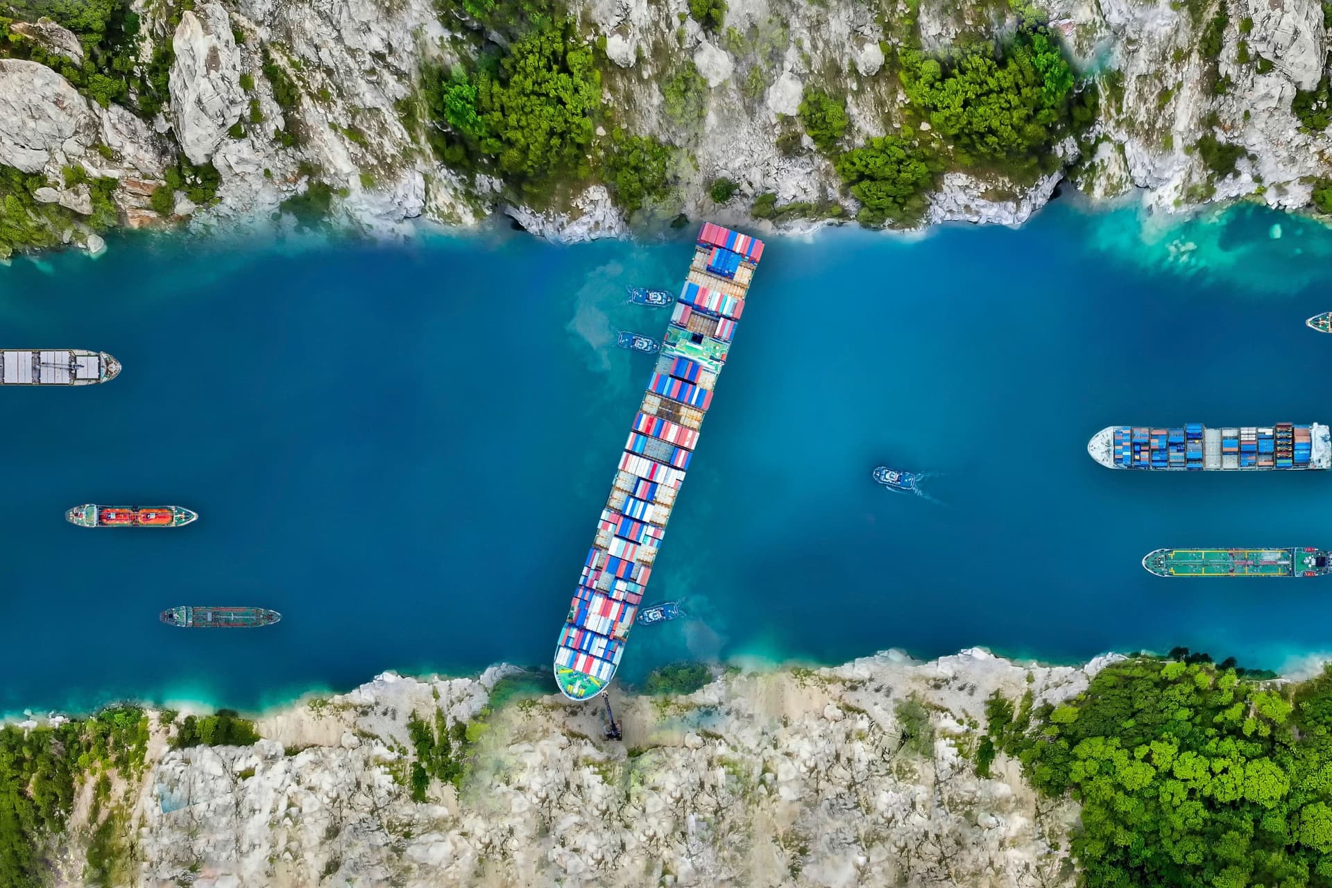 Luftaufnahme eins großes Frachtschiffs das quer in einem Kanal stecken geblieben ist und die Durchfahrt für andere Schiffe blockiert.