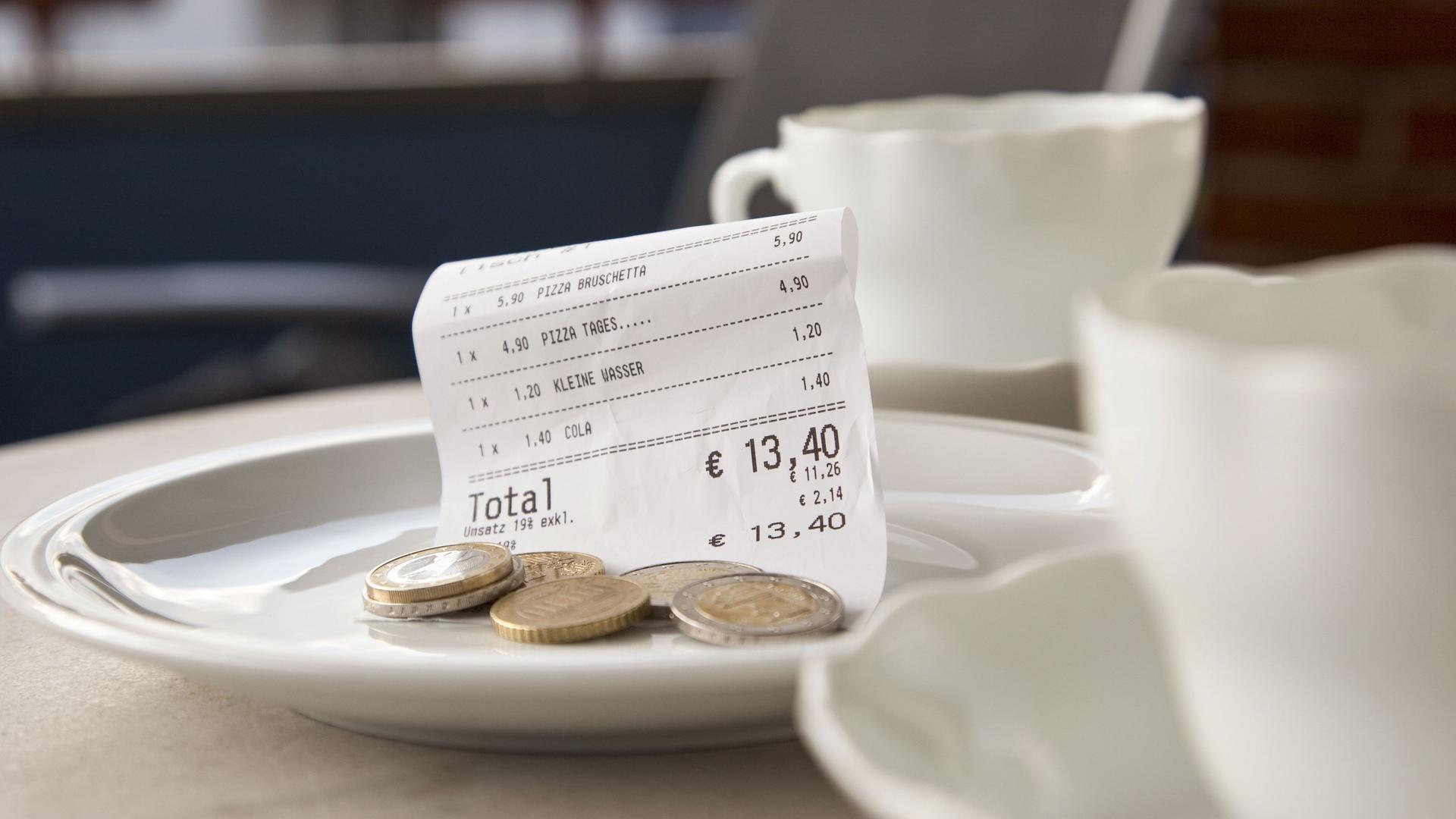 Zwei weiße Kaffeetassen stehen auf einem Restauranttisch. Trinkgeld liegt mit Rechnung auf dem Teller.