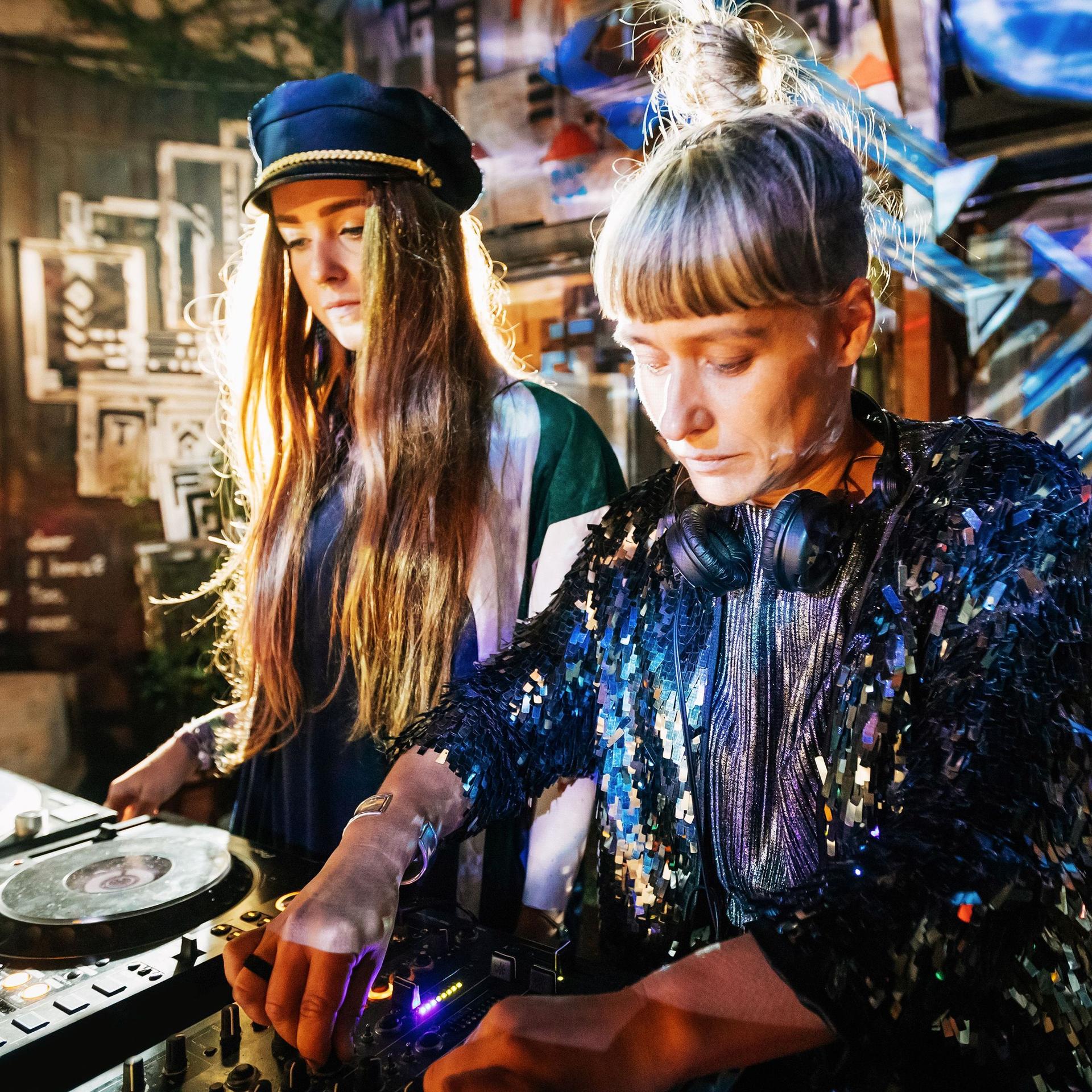 Zwei Frauen vor einem DJ-Pult in einem Club.
