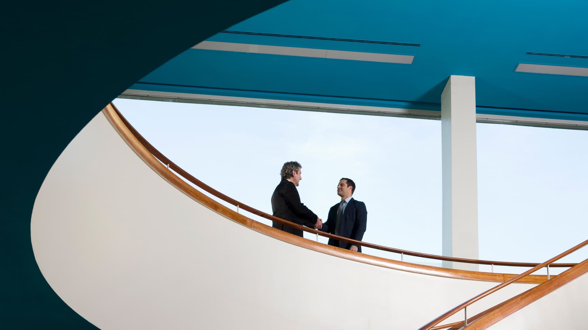 Zwei Geschäftsleute stehen auf einem Balkon und schütteln sich die Hände