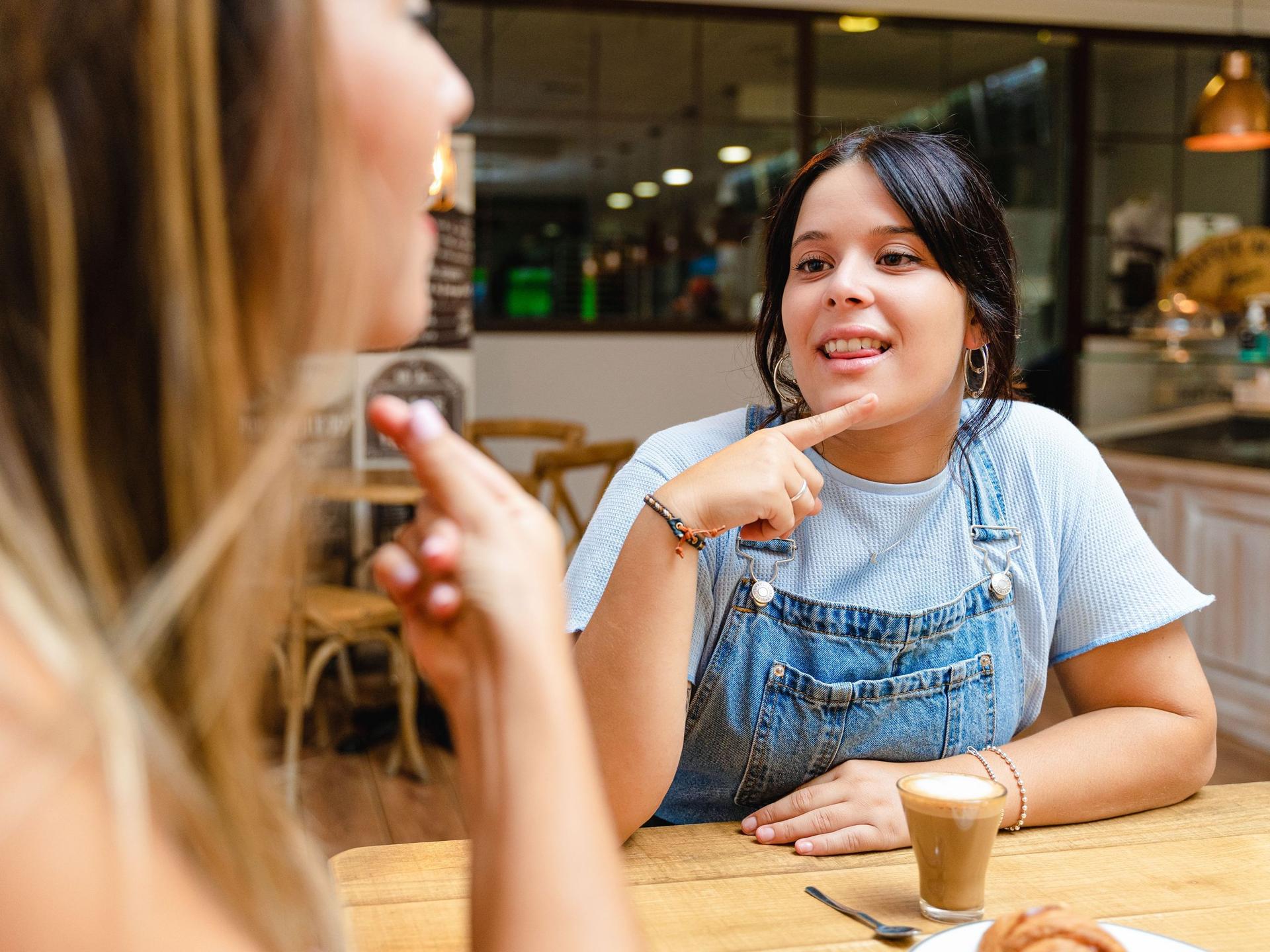 Zwei junge Frauen sitzen in einem Cafe und unterhalten sich in Zeichensprache.