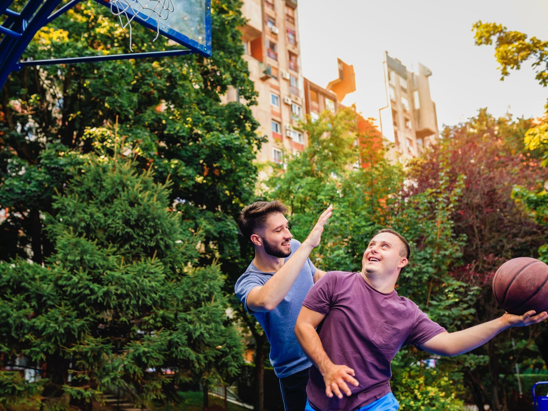Ein junger Mann mit Down-Syndrom spielt mit einem Freund Basketball.