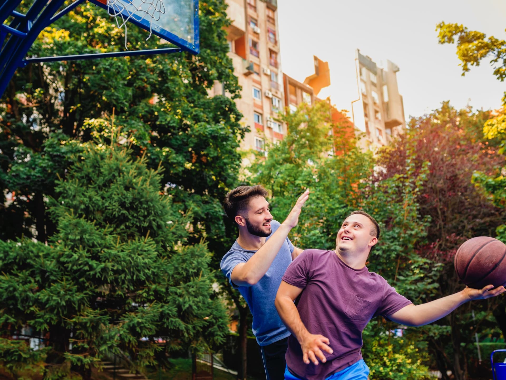 Ein junger Mann mit Down-Syndrom spielt mit einem Freund Basketball.