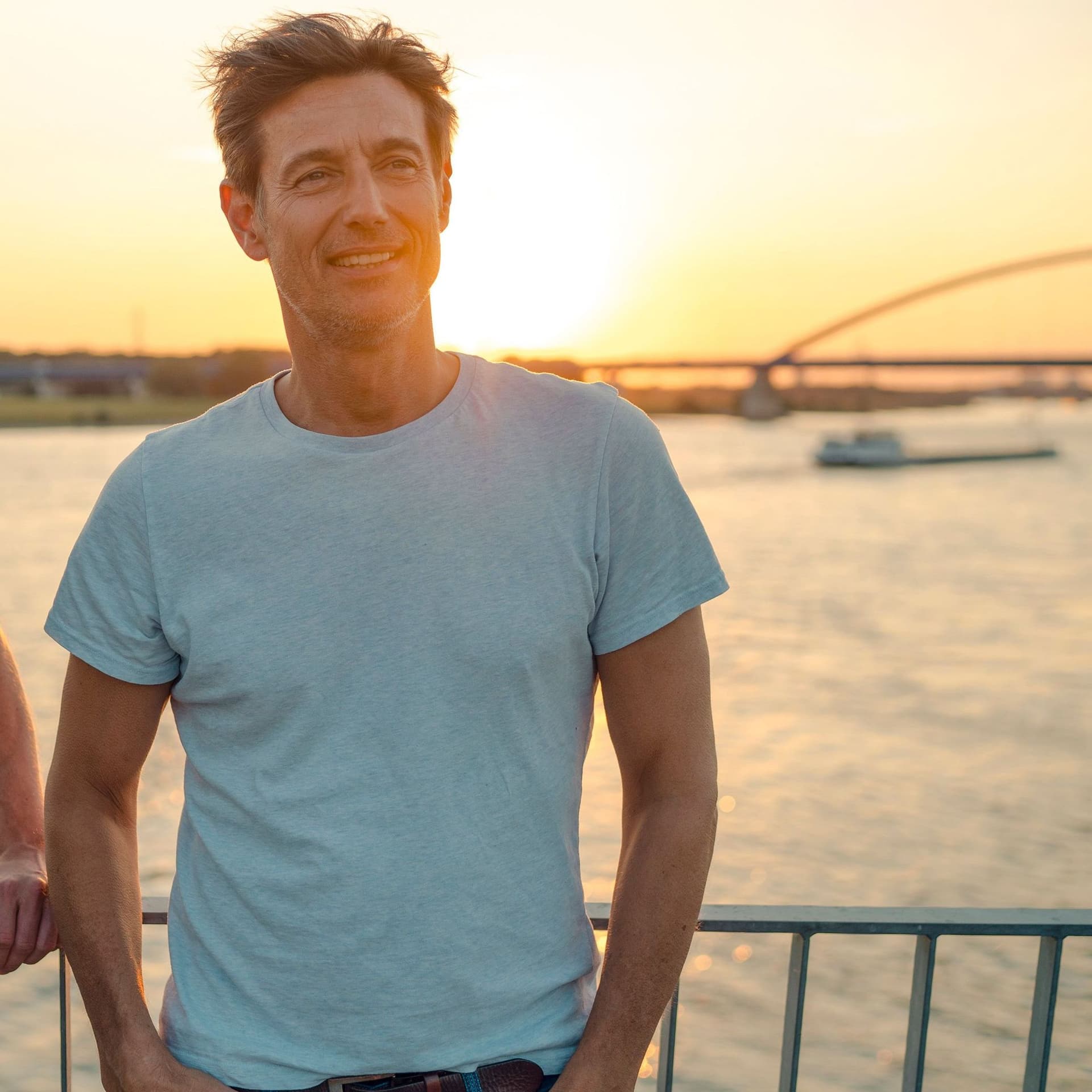 Zwei Freunde stehen auf einer Brücke über einem Fluß und unterhalten sich.