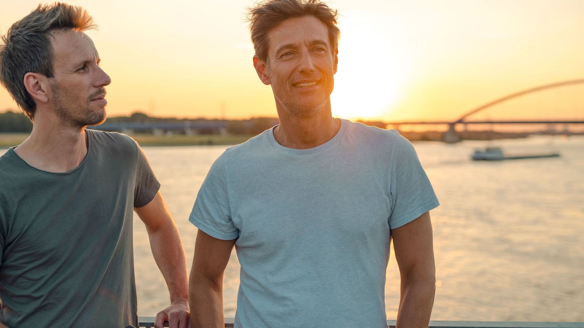 Zwei Freunde stehen auf einer Brücke über einem Fluß und unterhalten sich.