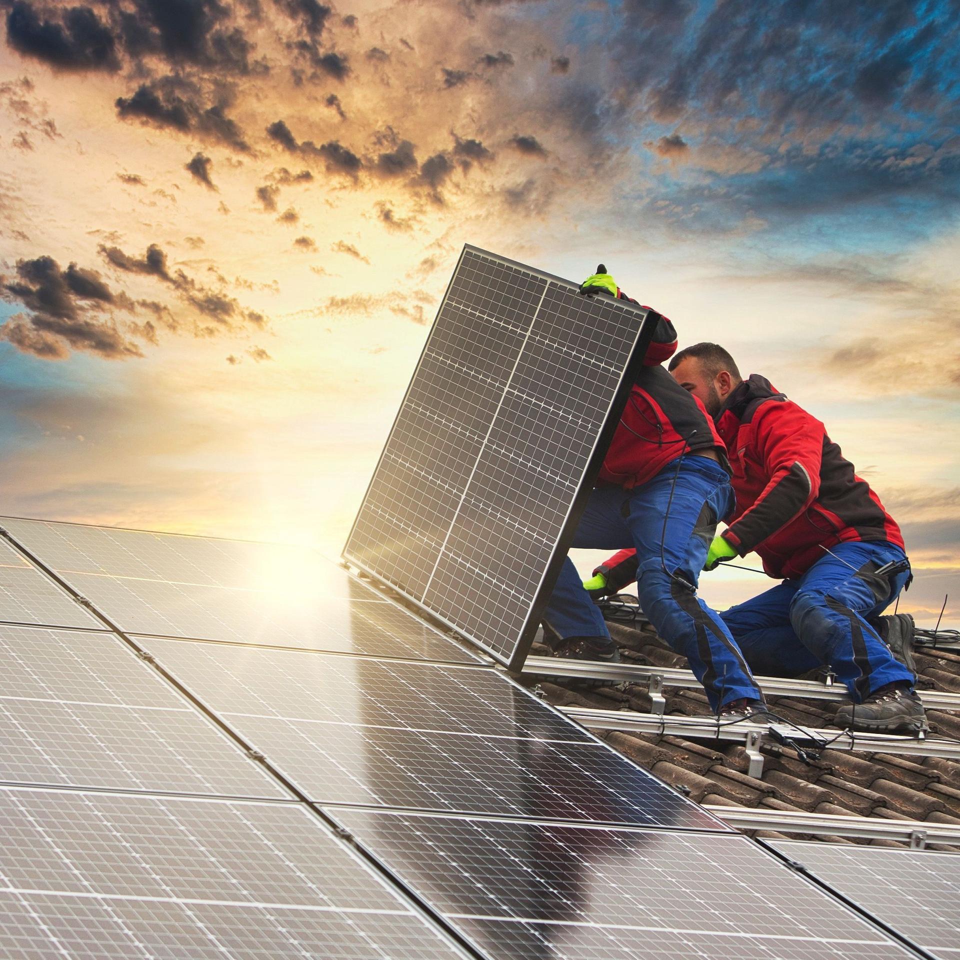 Zwei Männer installieren bei aufgehender Sonne Solarpanele auf einem Firmendach.