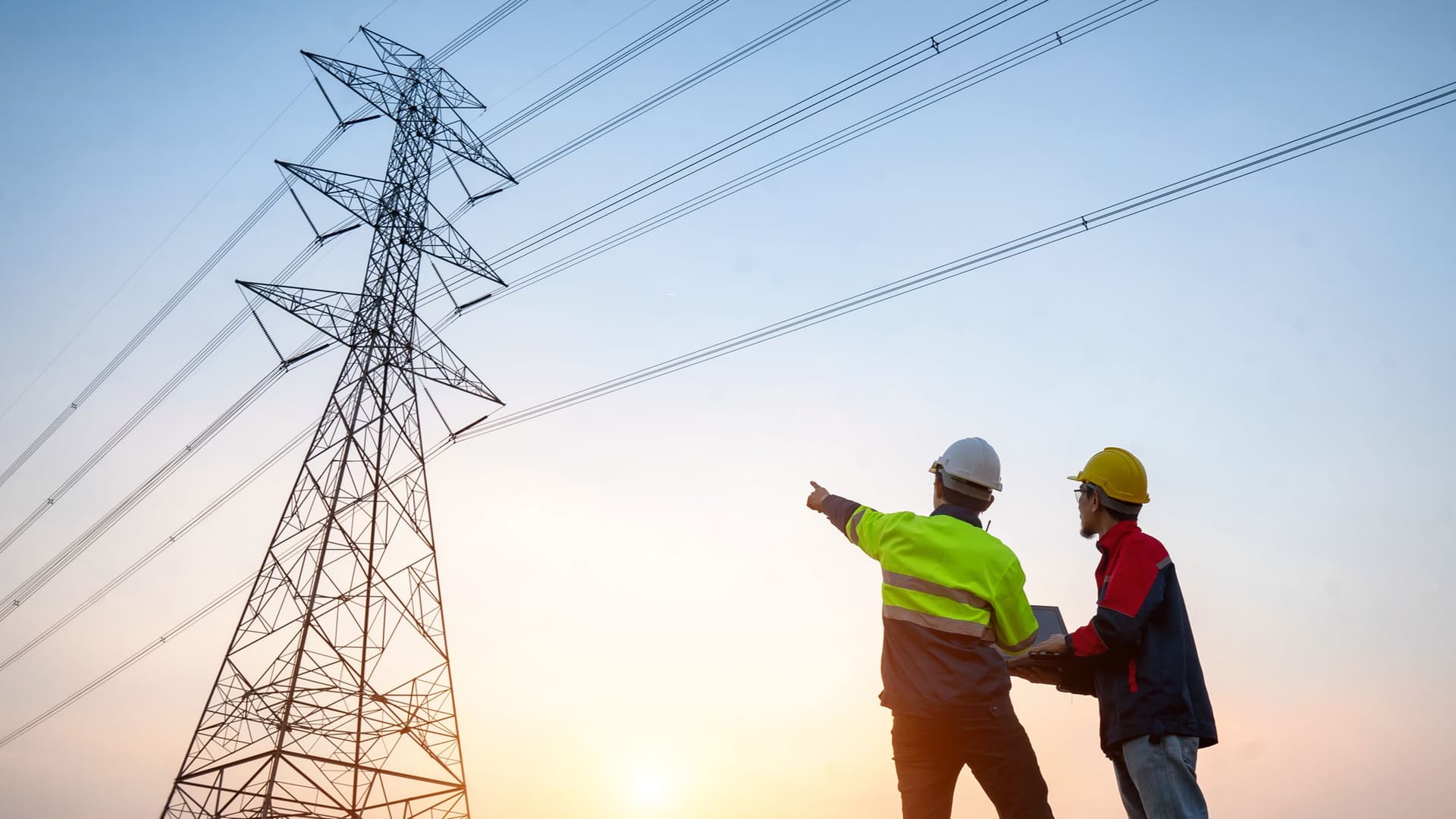Zwei Männer mit Helmen stehen draußen und einer zeigt auf einen Strommast