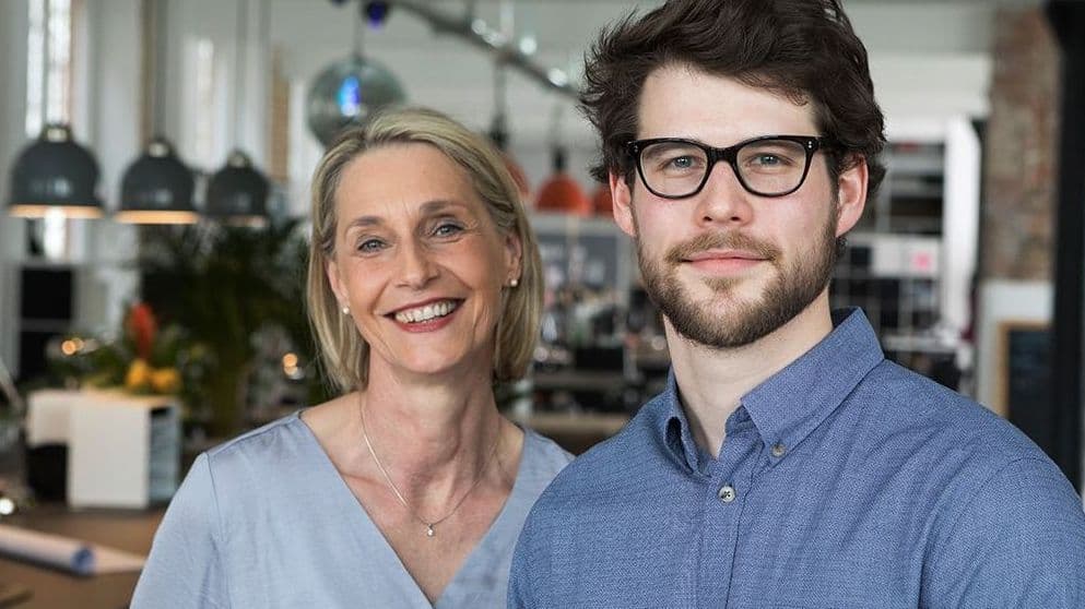 Zwei Personen stehen in einem Büro und schauen in die Kamera.