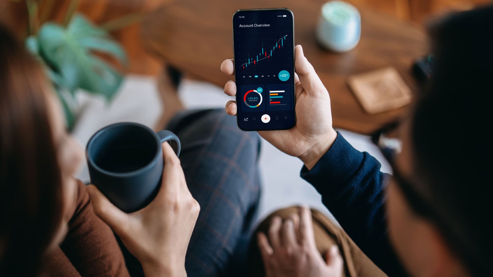 Zwei Personen trinken Kaffee und schauen auf die Börsenentwicklung am Handy.
