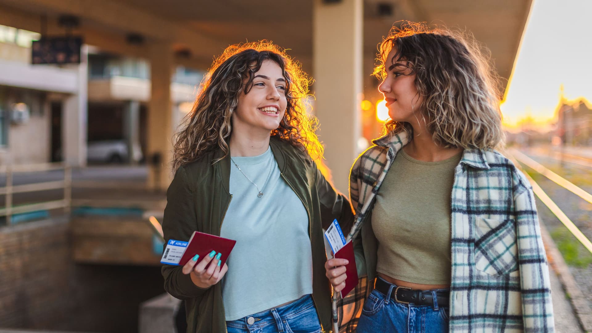 Zwei Teenager laufen lachend mit ihrem Reisepass in der Hand am Flughafen lang.