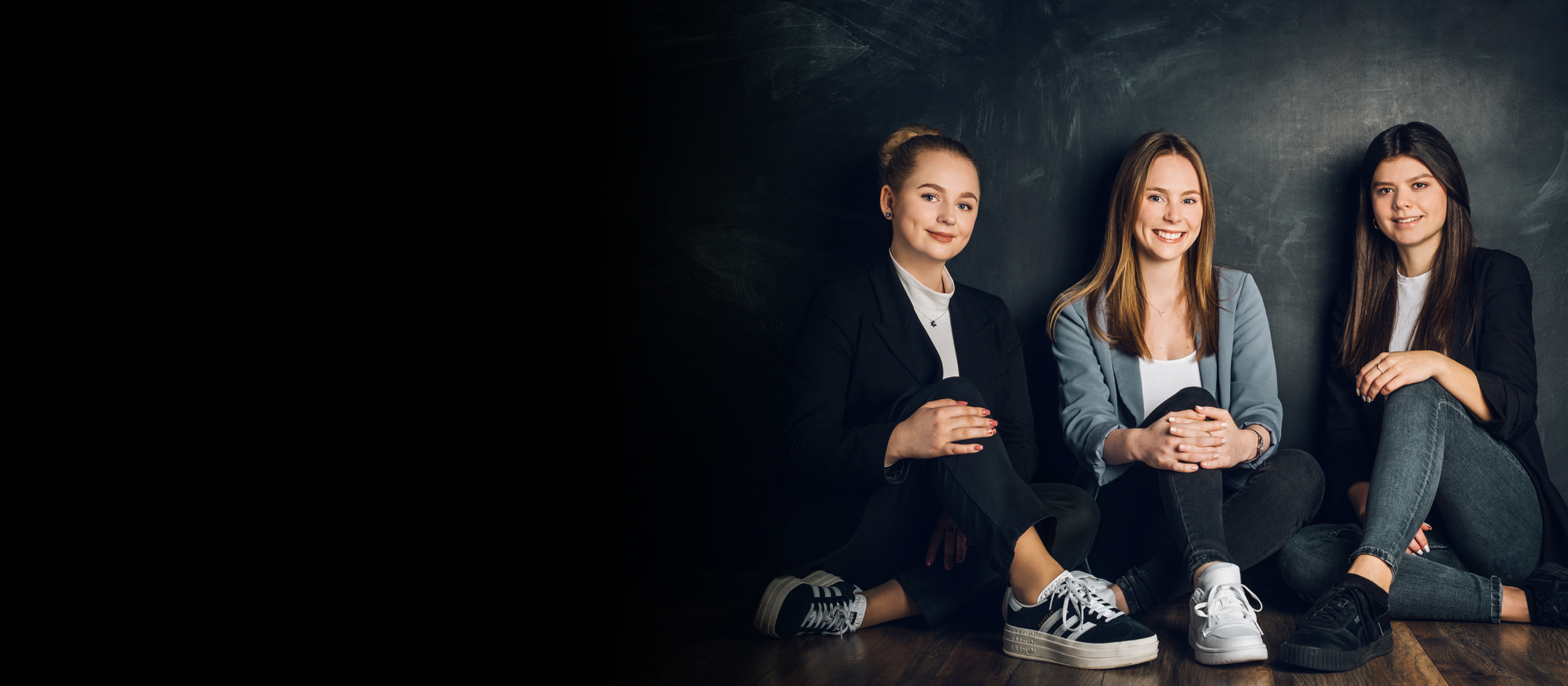 Drei der dualen Studentinnen sitzen vor einer Wand