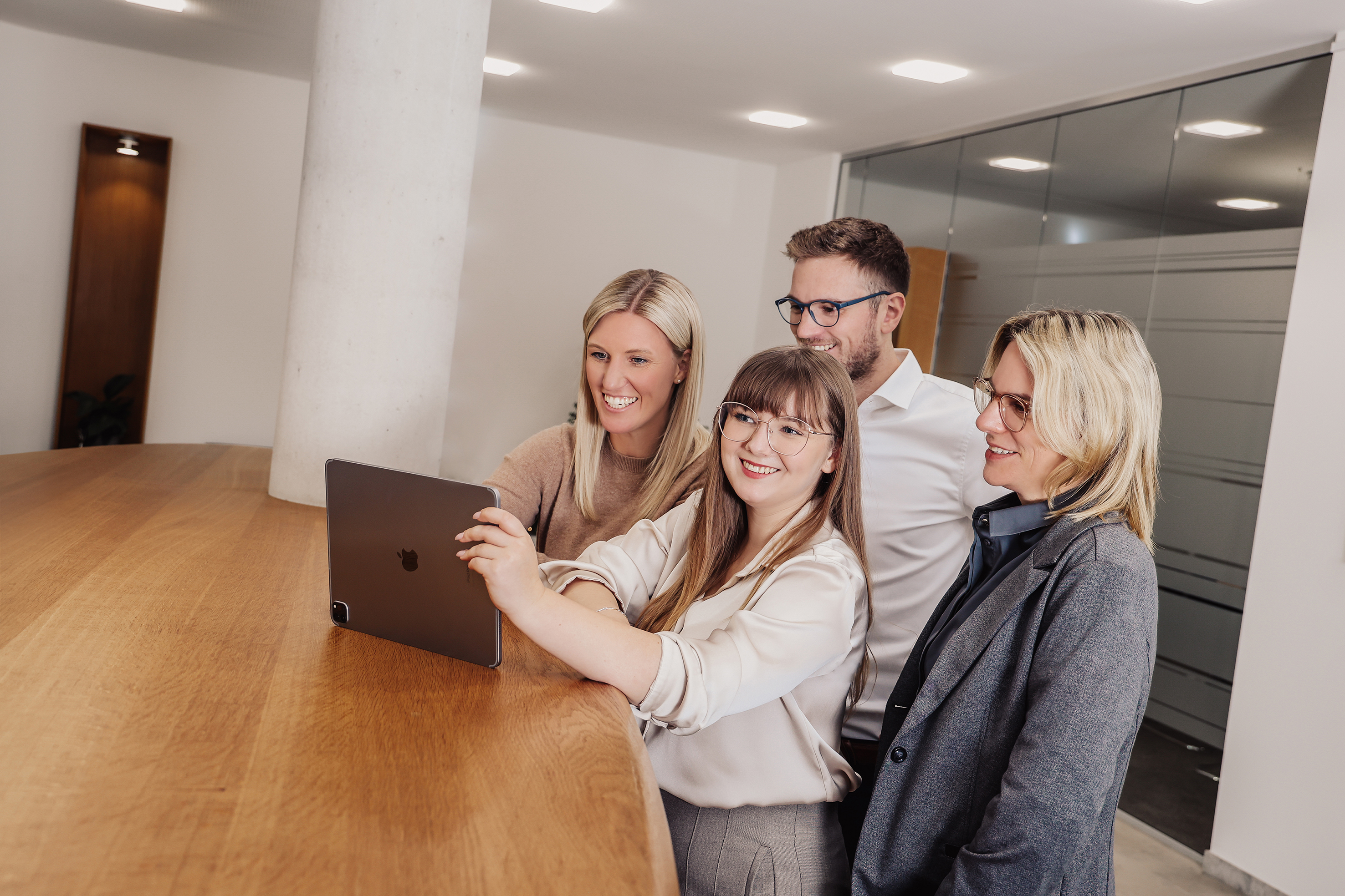 Gruppe on vier Mitarbeiten stehen am Tisch und arbeiten gemeinsam am Laptop