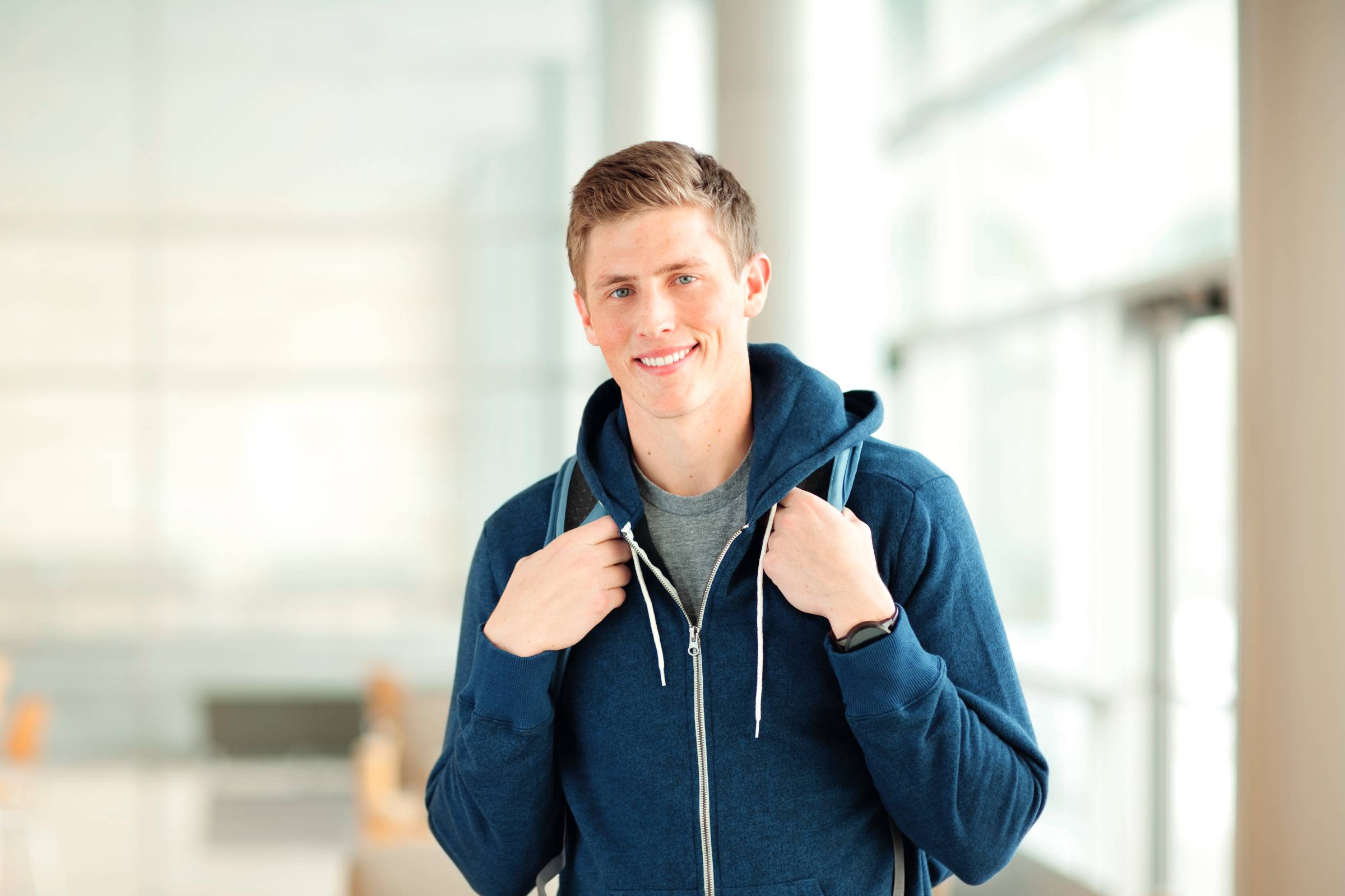 Ein junger Mann steht mit einem Rucksack auf dem Rücken im Klassenzimmer.