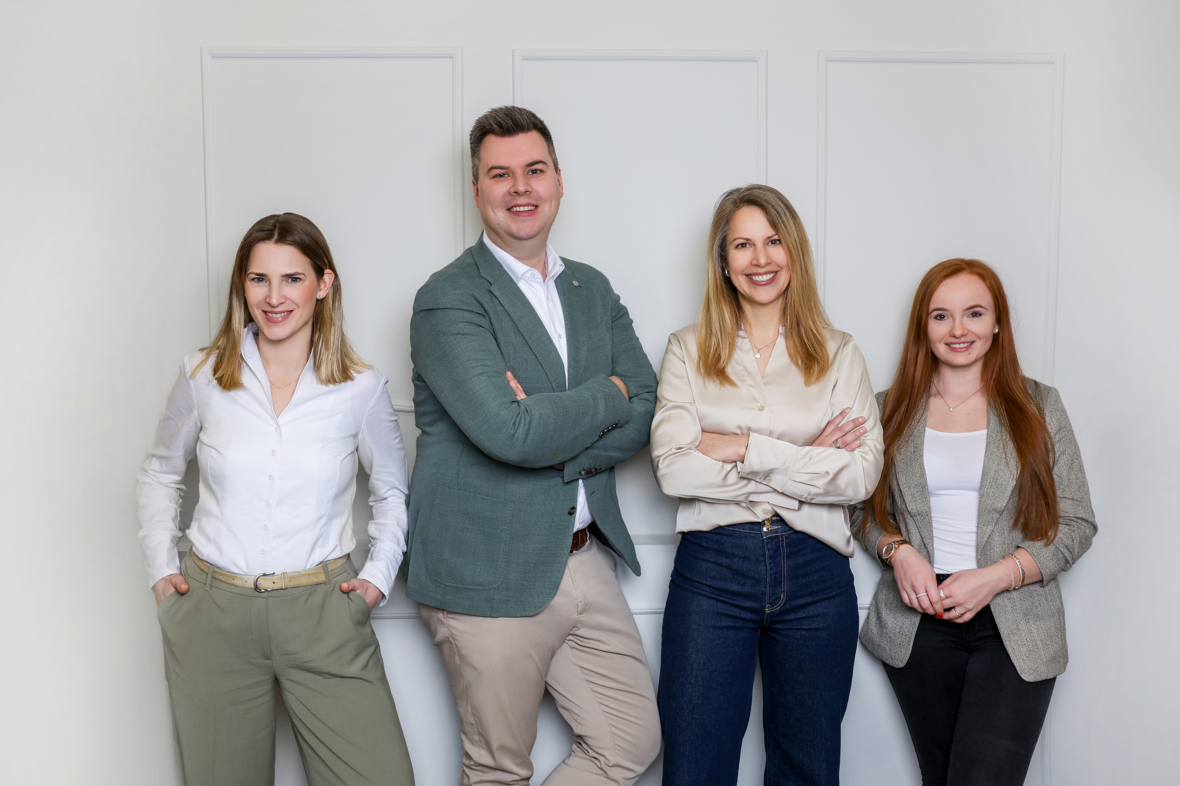Drei Frauen und ein Mann stehen als Team in einer Reihe vor einer Wand.
