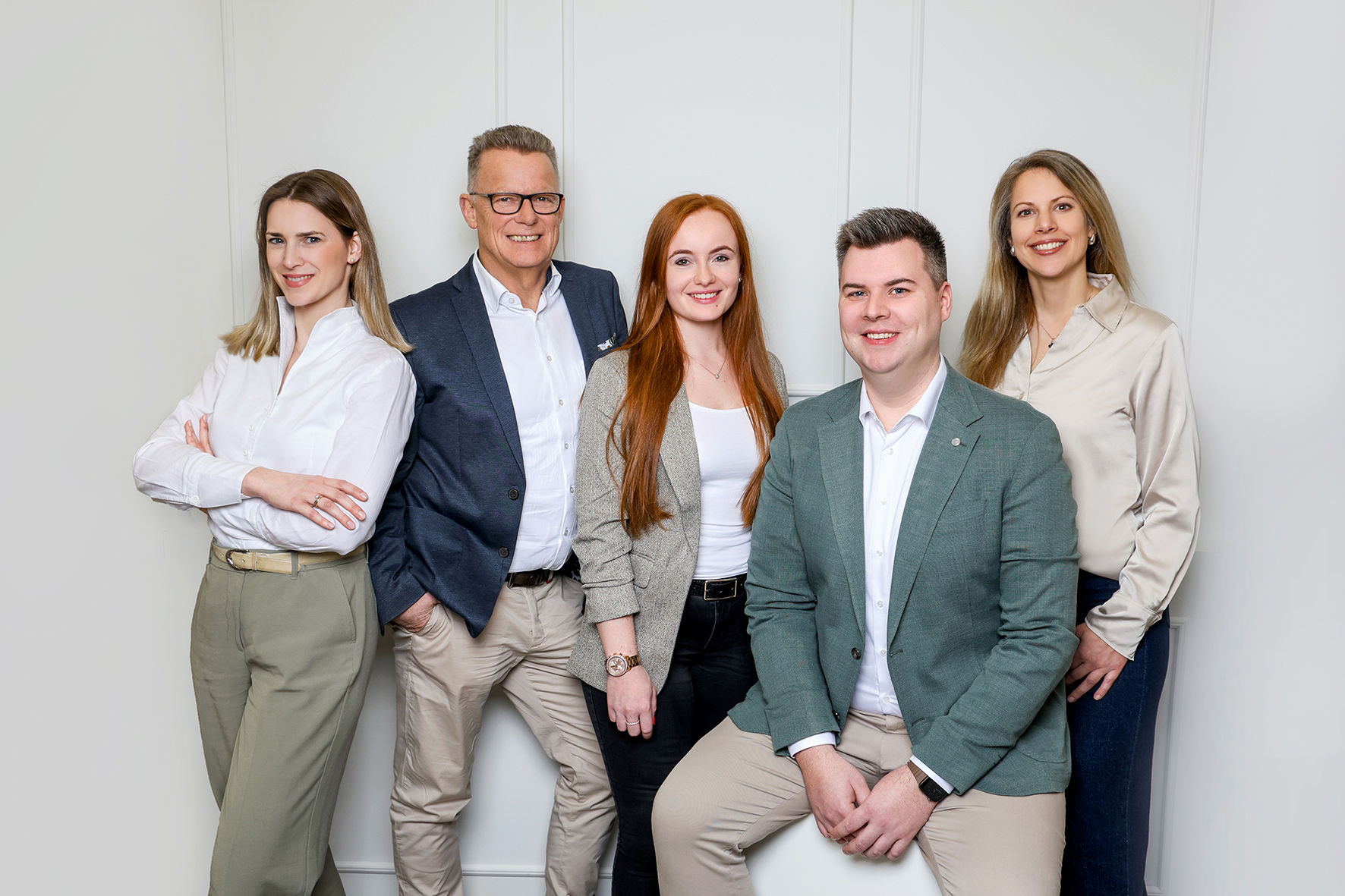 Team steht vor einer Wand. Drei Frauen und zwei Männer sind zu sehen.