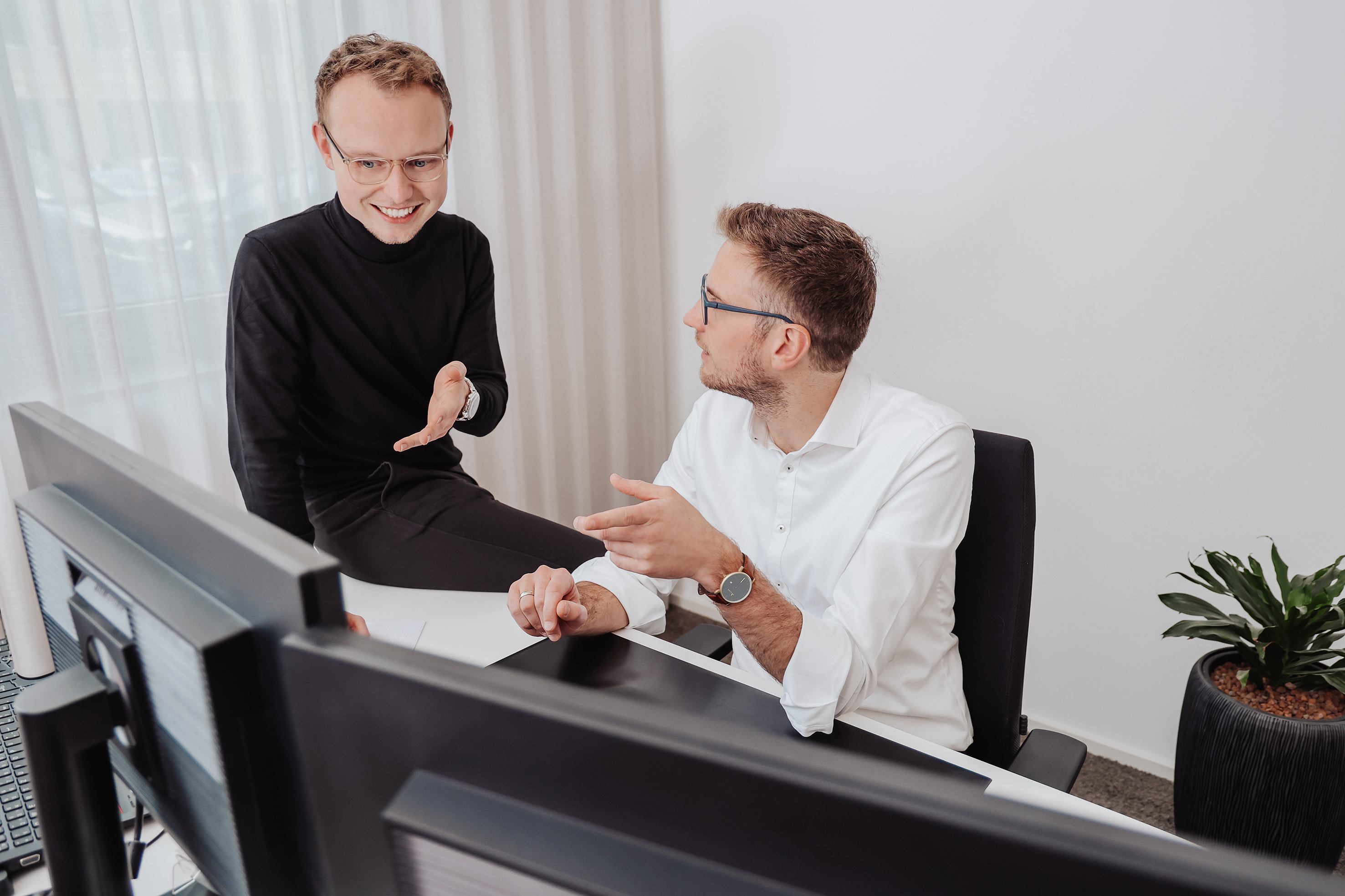 Zwei  Männer sitzen am Schreibtisch und stimmen sich ab.