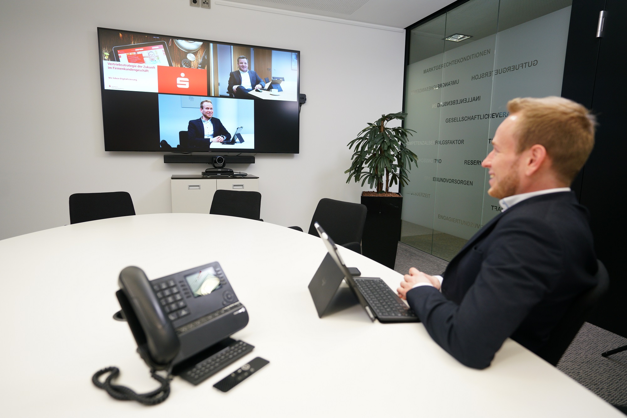 Mann nimmt an einem Meeting teil und sieht Teilnehmer auf einem Fernseher. 