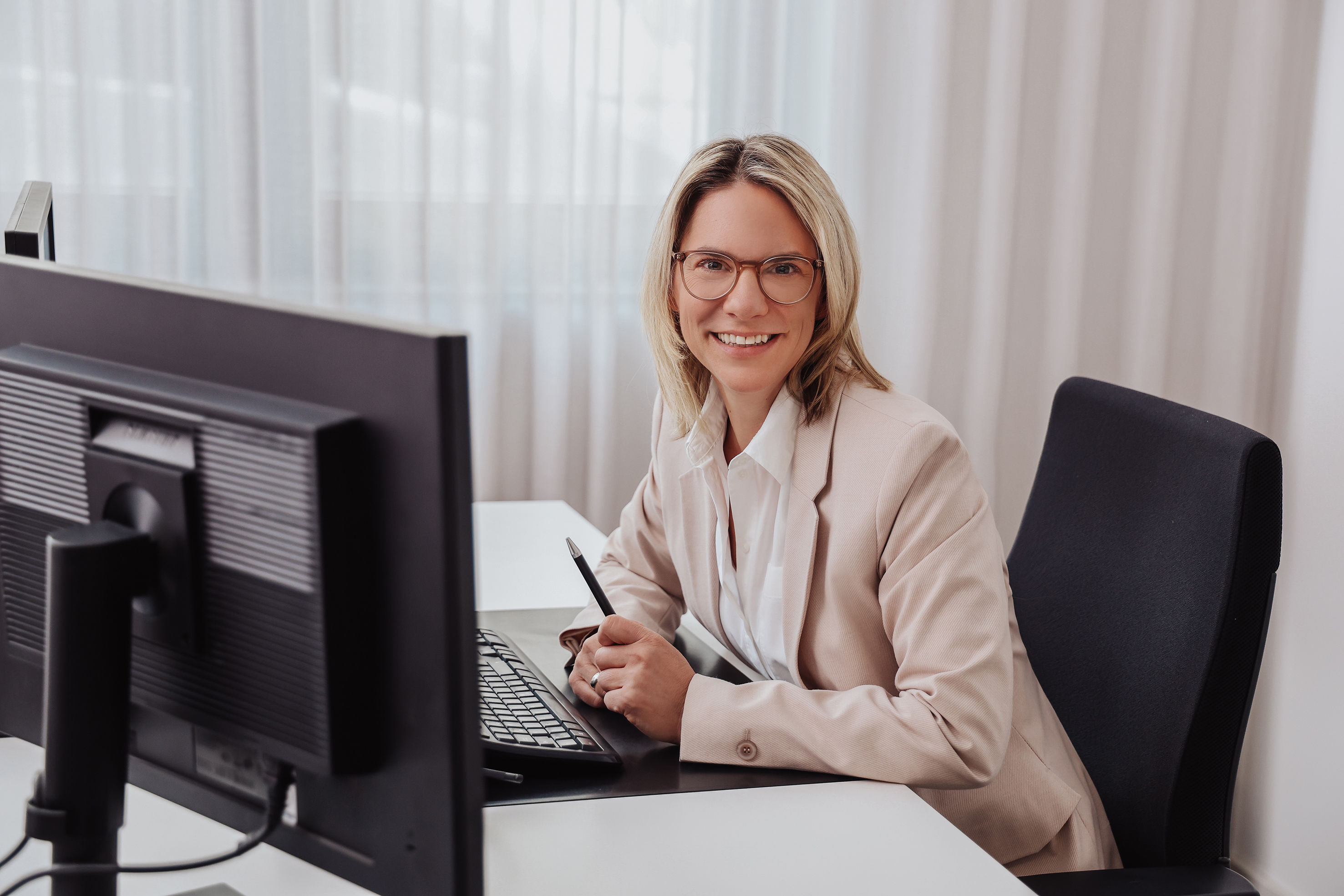 Frau sitzt am PC am Schreibtisch und lächelt in die Kamera